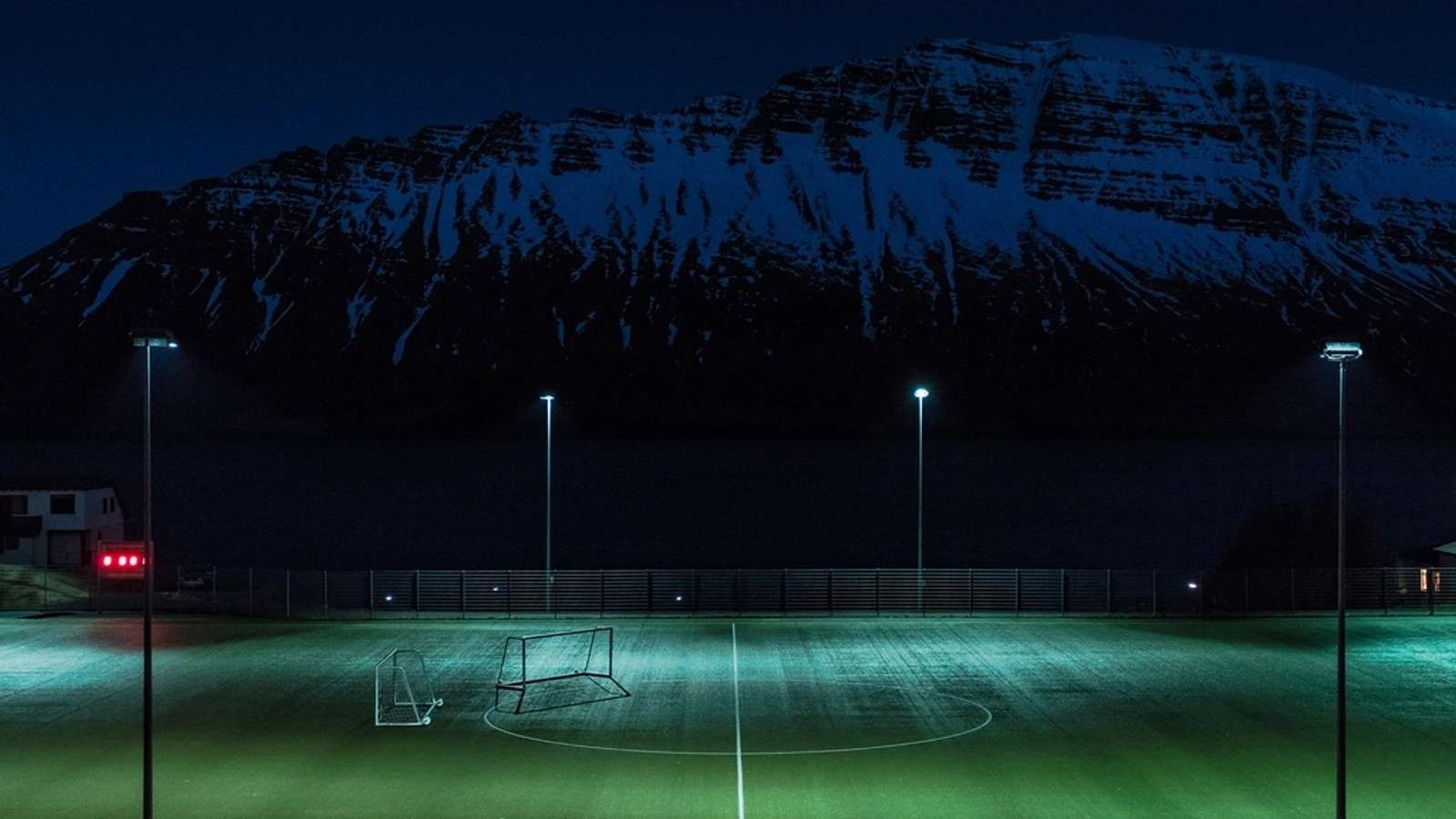 Floodlit pitch at dusk beneath a mountain ridge